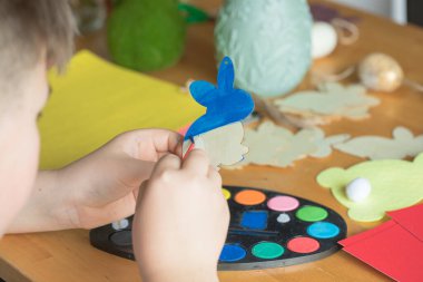 Küçük çocuk evde ahşap Paskalya tavşanı çiziyor.