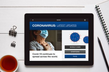 Coronavirus, beyaz ahşap masadaki ofis eşyalarıyla yatay tablet ekranda son haberler. Üst görünüm