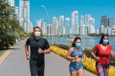 Tıbbi koruyucu maskeli bir grup sporcu güneşli bir parkta sabah karantinada, Coronavirus 'ta koşuyor.