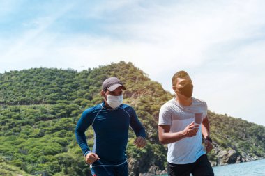 Sabahleyin maskeli adamlar sahile doğru koşuyor. Sahilde koşan sağlıklı erkek sporcular..