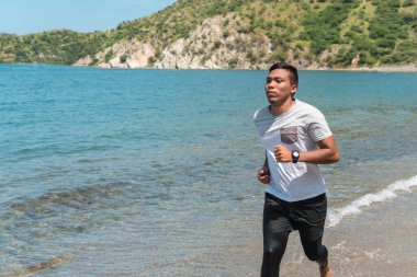 Denize ya da okyanusa yakın tropikal bir kumsalda koşuyor..