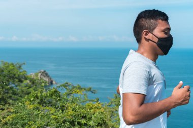 Formda kal. Salgın sırasında dağlarda koşan tıbbi maskeli genç bir Afro-Amerikalı atlet. Spor ve koronavirüs. Covid-19. Korunma. Sağlık kavramı