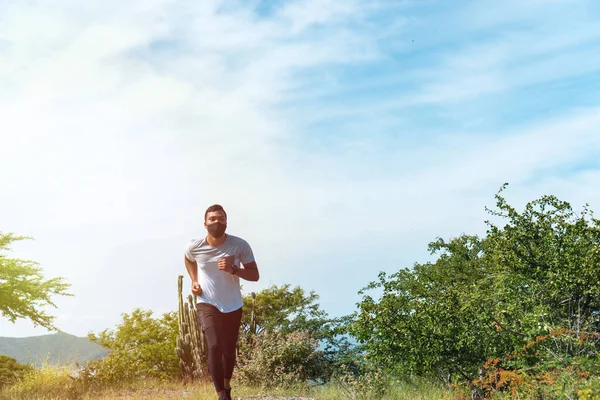 Running during quarantine. A young African athlete in sportswear and a medical protective mask running through the mountains in the morning. Healthy habits. Sports. Coronavirus