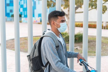 Tıbbi maskeli bir adam bisikletinin yanında yürüyor.