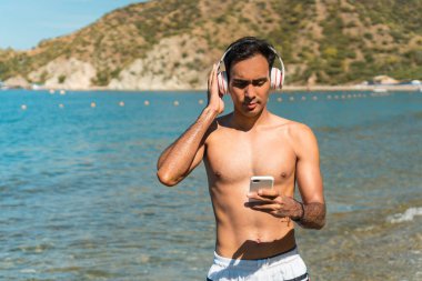 Sahilde kulaklıkla müzik dinleyen genç bir adam.