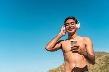 Genç bir İspanyol çocuk plajda kulaklıkla müzik dinliyor.