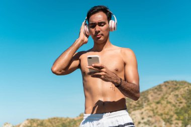 Sahilde kulaklıkla müzik dinleyen genç bir adam.