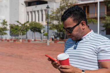 Parkta elinde kahve fincanı ve cep telefonu olan bir adamın portresi.