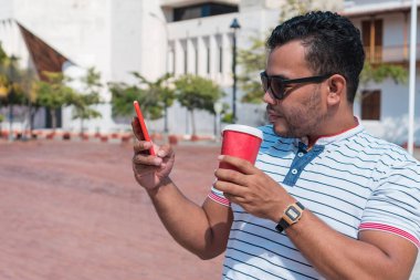 Parkta elinde telefon ve kahve tutan bir adam.