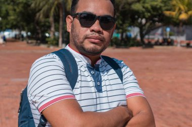 Güneş gözlüklü sıradan bir genç. Sırt çantası kameraya dönük şekilde sokakta yürüyor.