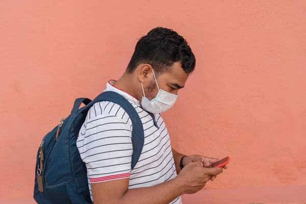 A young man with a protective mask checks his cell phone as he walks through the city streets