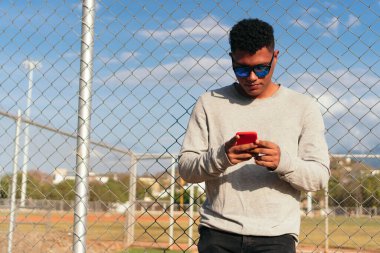 Portrait of a young man wearing a gray T-shirt, cell phone and sunglasses outdoors.