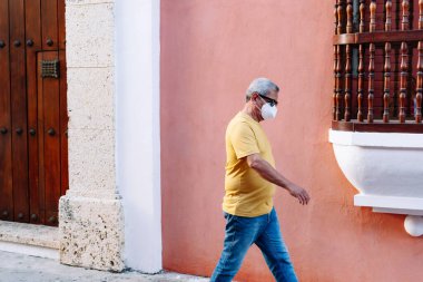 Caddede yürüyen koruyucu maskeli yaşlı bir adam.