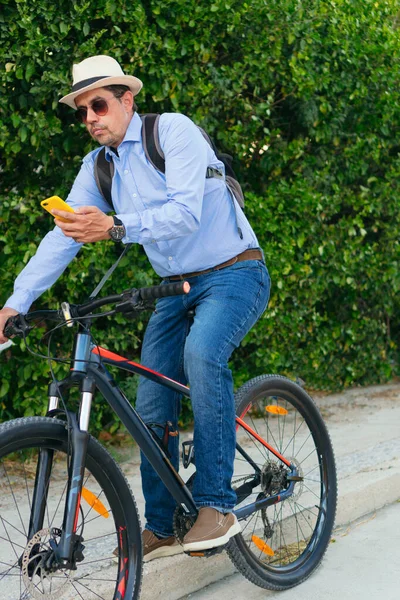 カジュアルな服を着たラテン系アメリカ人のビジネスマンが自転車に乗っている間に携帯電話をチェックする — ストック写真