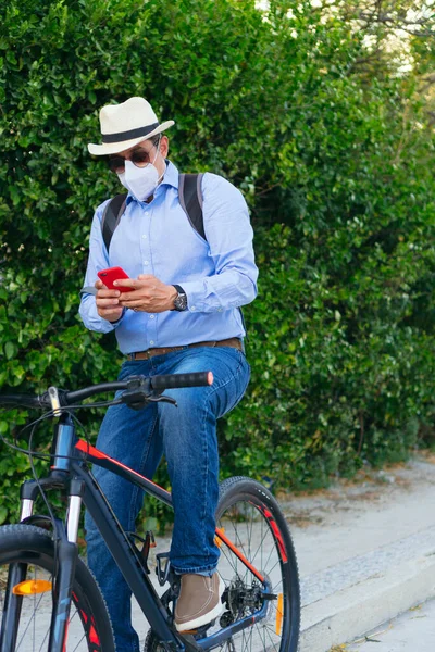自転車に乗っている間 保護マスクチェック携帯電話を身に着けている男 — ストック写真
