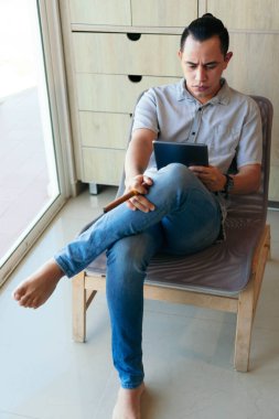 Oturma odasında elinde puroyla oturan bir adam evden çalışmak için tablet kullanıyor.