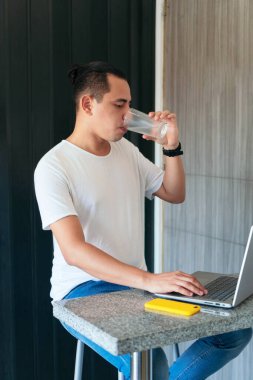 Adam evde dizüstü bilgisayarında çalışırken su içiyor.
