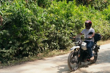 Kasklı bir adam, yüksek hızda sürüyor. Arkasında bulanık yeşil bir arka plan var..