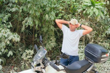 Motosikletin yanında gündelik giysiler içinde Latin kökenli ciddi bir motosikletçi.