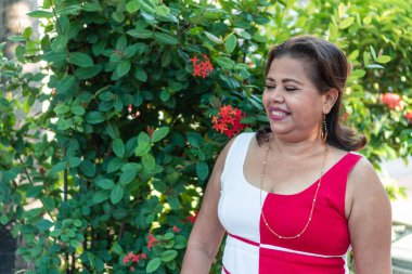 50 'li yaşlarda Latin bir kadın kırmızı çiçekle güneş ışığında poz veriyor.