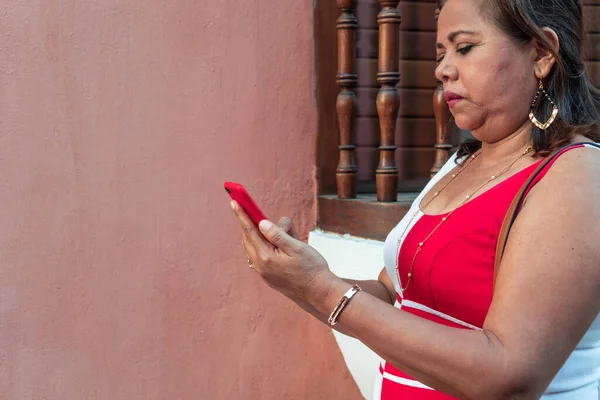 Older Hispanic woman typing a message on her smartphone while walking down the street