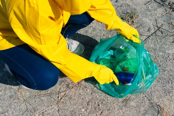 Woman in raincoat picking up trash in park