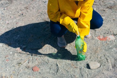 Plastik eldivenli tanınmayan bir kadın parktan plastik şişe alıyor.