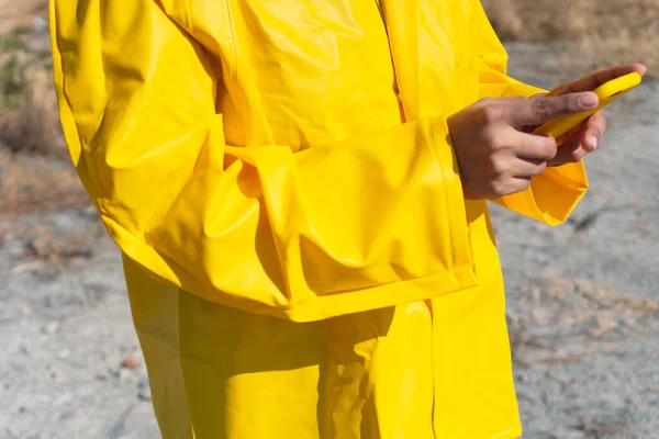 Young woman in raincoat walking outdoors, checking her cell phone