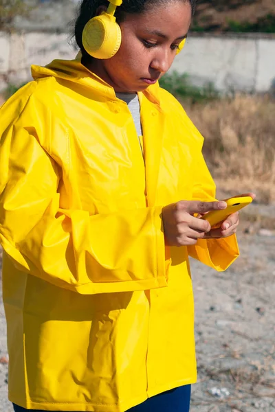 Girl in raincoat walking past outdoors, checking her cell phone