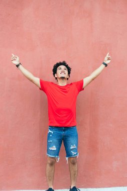 Yakışıklı genç İspanyol adam kırmızı duvarın önünde dikilirken gülümsüyor.