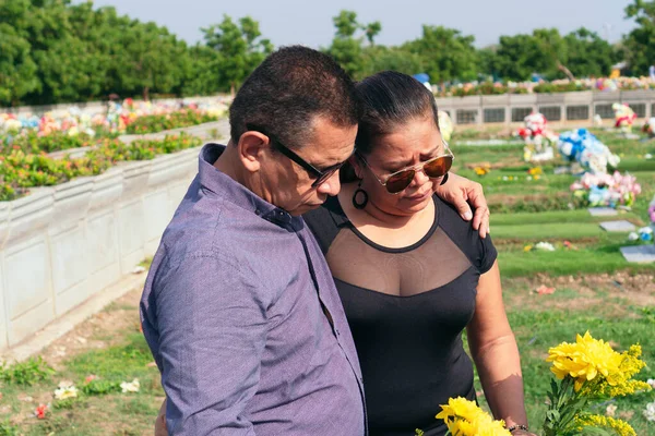 Ellerinde çiçeklerle mezarlıkta dikilen yas tutan çift..