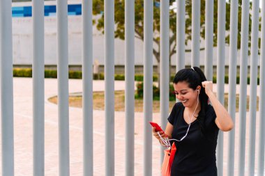 Parkta cep telefonunu kontrol eden sportif bir kadın.