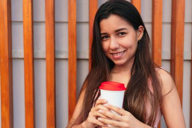 Güzel genç bir kadın elinde bir bardak kahveyle kameraya bakıyor..