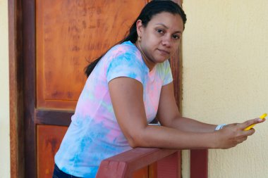 40 yaşını geçmiş İspanyol bir kadın, elinde cep telefonu var. Evinin önünde bir uygulama kullanıyor..