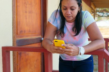 Latin bir kadın evinin dışında cep telefonunu kontrol ediyor.