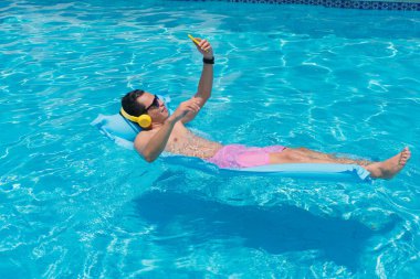 Young Latino man at the pool using his cell phone.