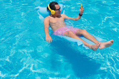 Young man at the swimming pool using his cell phone.