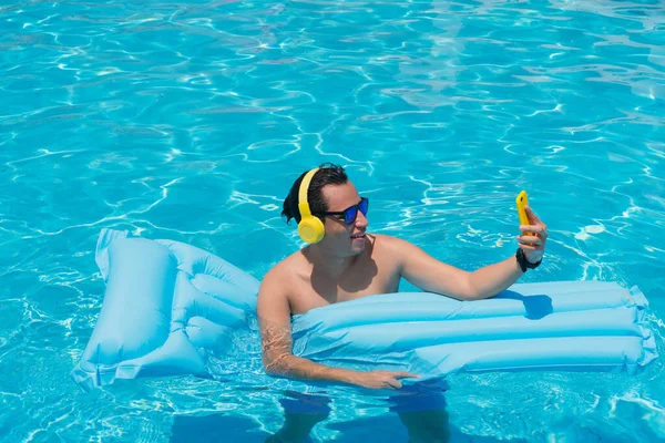 Man sunbathing by the pool and holding cell phone in his hand