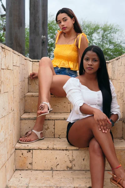 Güzel Latin kadınlar parkta merdivenlerde oturuyor.