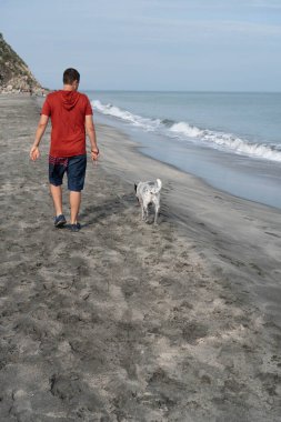 Sırtüstü yatan bir adam sabah sahilde bir köpeği gezdiriyor.