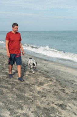Latin bir adam sabah sahilde bir köpeği gezdiriyor.