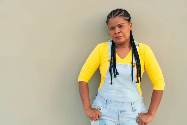 Ciddi bir Afrikalı Amerikalı kadın gri duvara yaslanıyor.