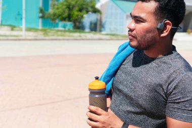 Fitness adamı parkta dikilirken su şişesi kullanır. Neşeli sporcu parkta mola veriyor..