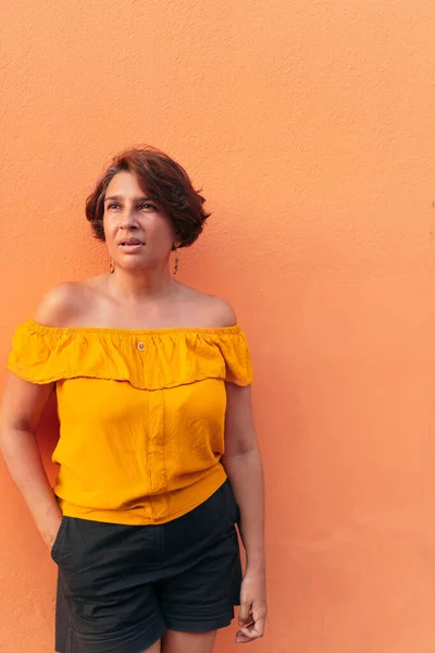 Turuncu duvarda sarı bluzlu olgun bir kadın.