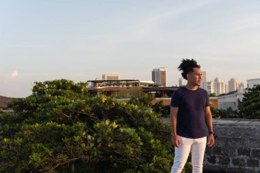 Şehir siluetine tepeden bakan afro saçlı bir adam çatıda duruyor.