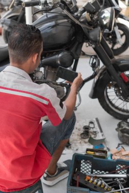 Tamirci atölyede motosiklet tamir ederken akıllı telefonu kontrol ediyor.