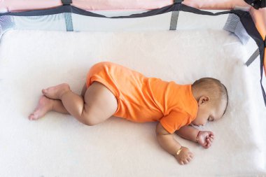 Bebek karyolada huzur içinde uyuyor, turuncu tulum giyiyor.