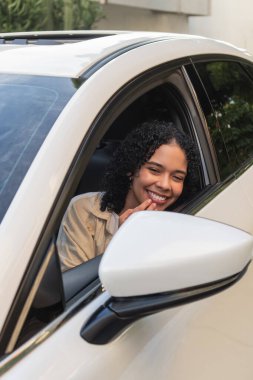 Yeni beyaz arabasını sürerken gülümseyen genç bir kadın.