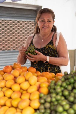 Kadın açık pazardaki tezgahtan taze meyve seçiyor.