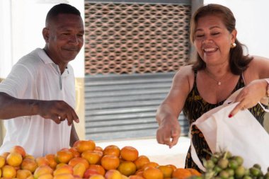 Adam açık hava pazarında mutlu bir kadına taze meyve satıyor.